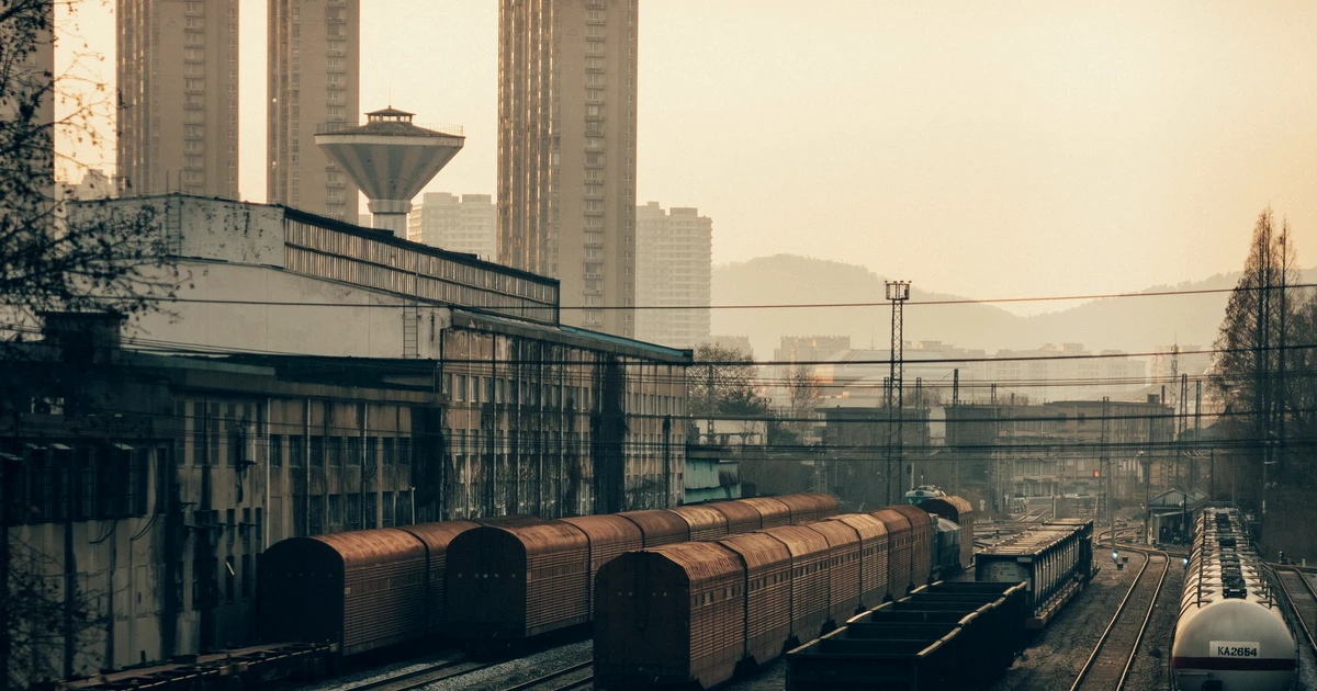 Pátio ferroviário industrial com vagões de carga ao pôr do sol e prédios ao fundo