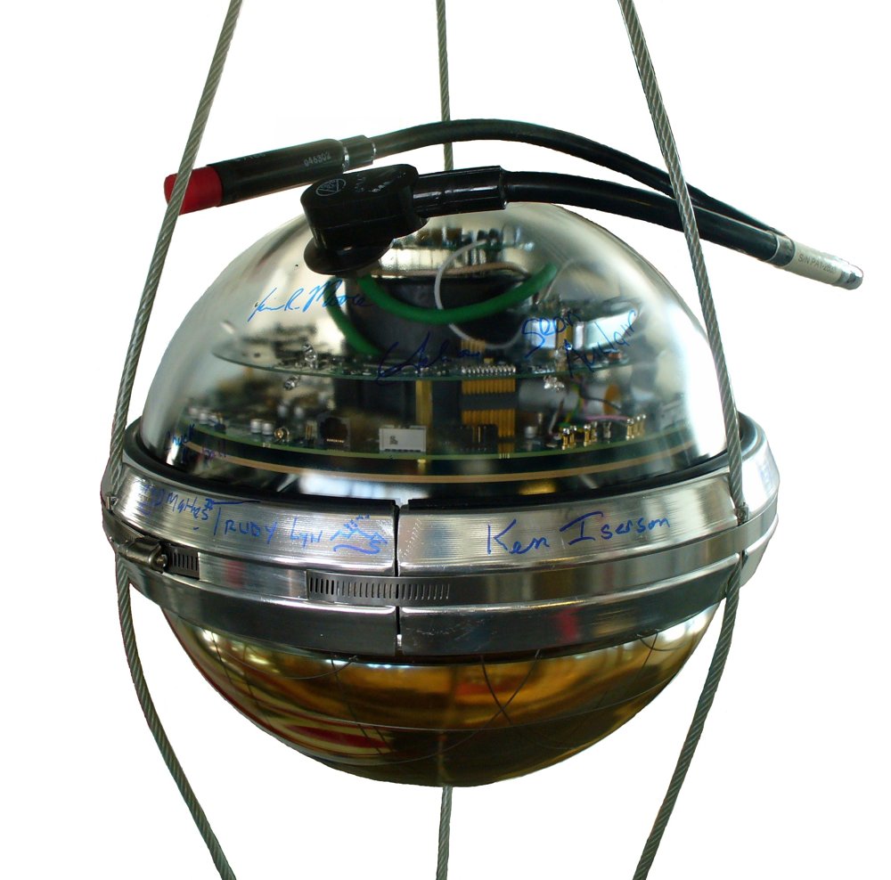 Esfera de vidro transparente do tamanho de uma bola de basquete, com placas de circuito visíveis por dentro, presa por cabos de aço e com assinaturas escritas à caneta na faixa metálica do meio