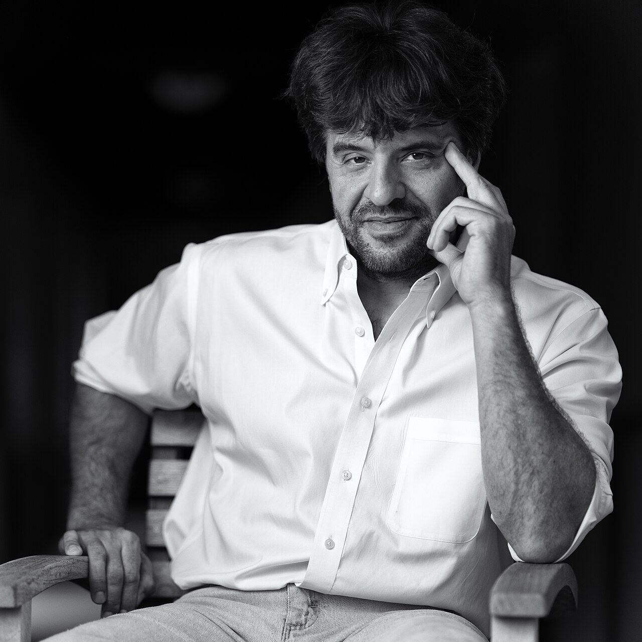 Retrato em preto e branco de Karl Deisseroth, homem de cabelo escuro e barba, de camisa branca, sentado numa cadeira de madeira
