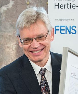 Retrato de Peter Hegemann, homem de cabelos brancos, óculos e terno escuro, sorrindo