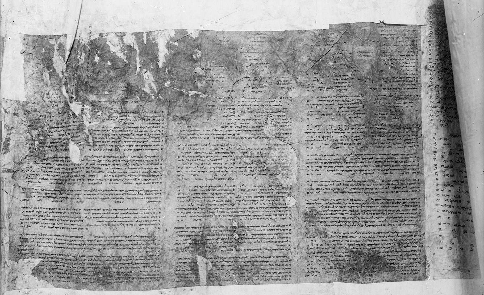 Fotografia em preto e branco de um rolo de pergaminho antigo e gasto, com colunas de texto em escrita samaritana
